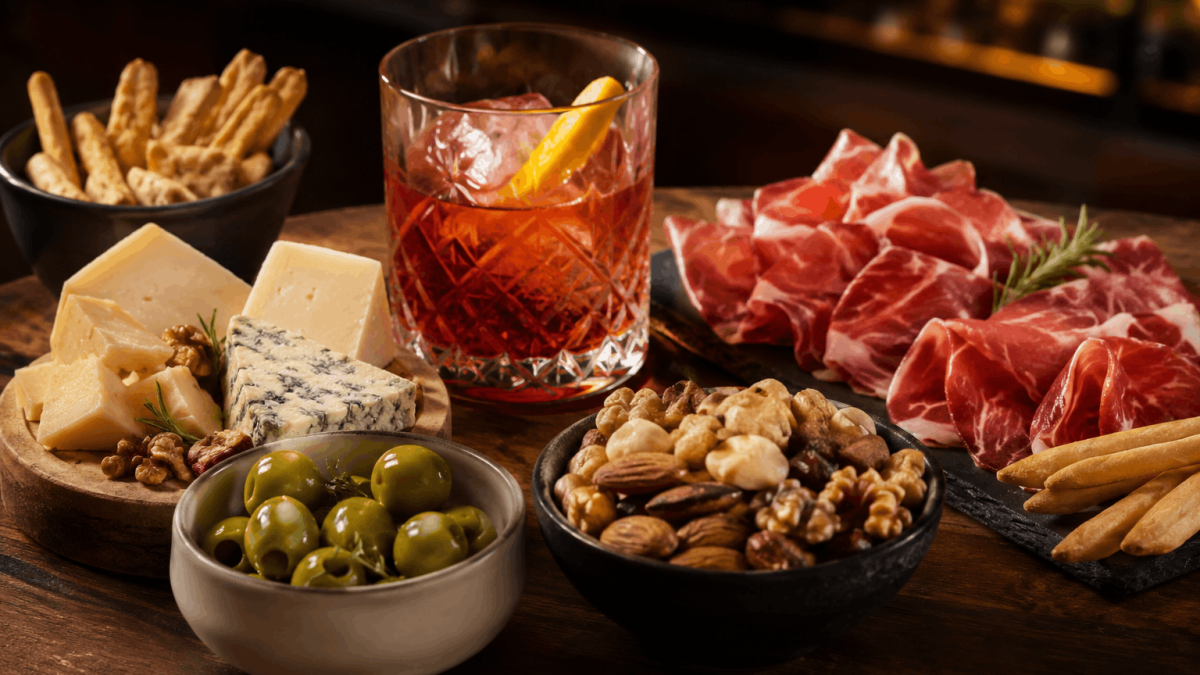 Selección de snacks gourmet para acompañar un cóctel con aceitunas, quesos, jamón y frutos secos.